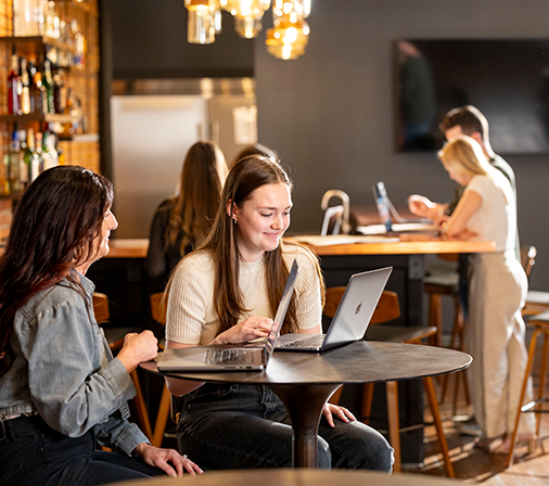 multiple people sitting and looking at laptops in a cafe