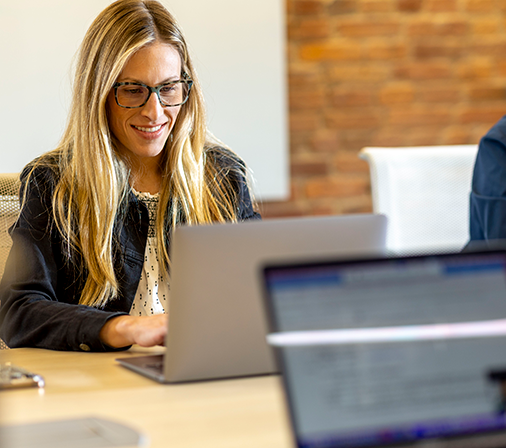a sitting woman smiling and looking down at a laptop