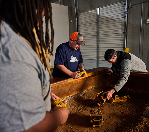 Three people looking over a diorama of small scale caterpillar equipment