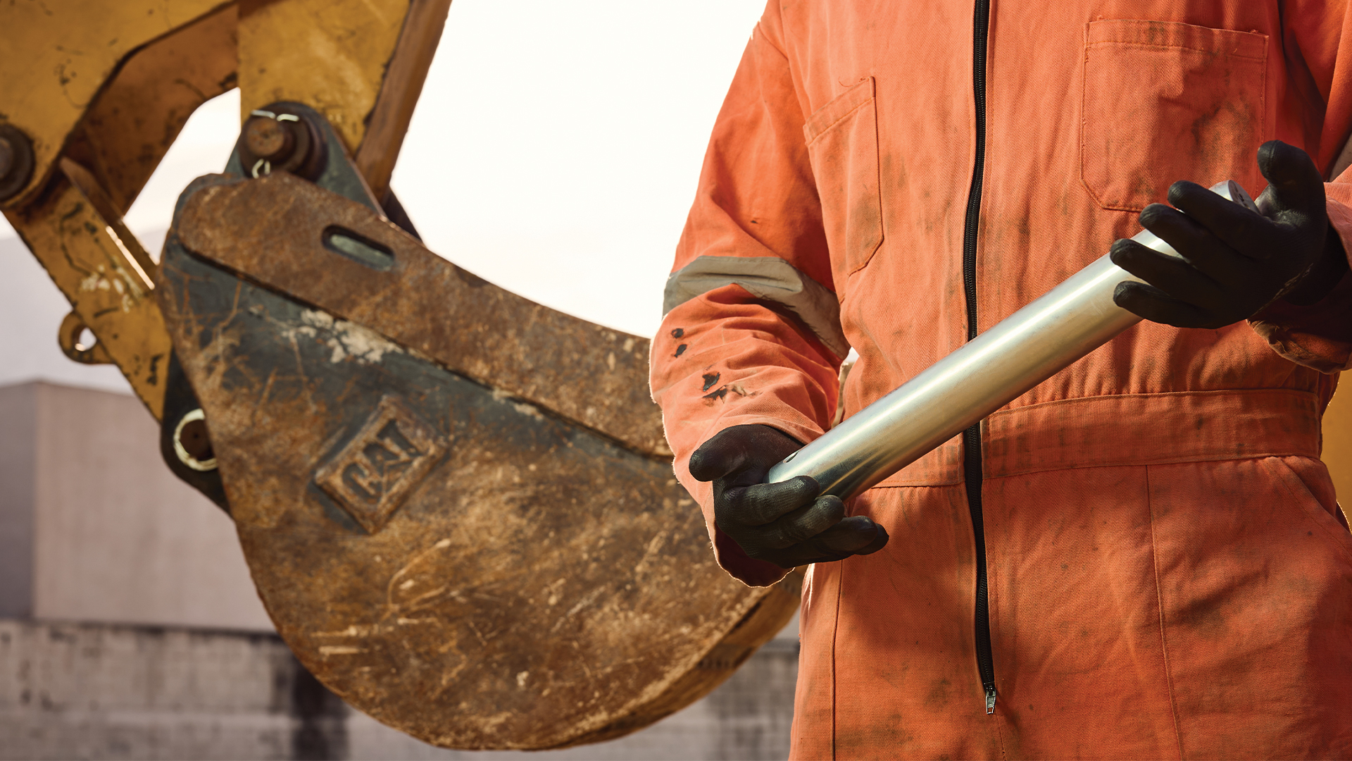 Worker holding an equipment part beside a Cat excavator.