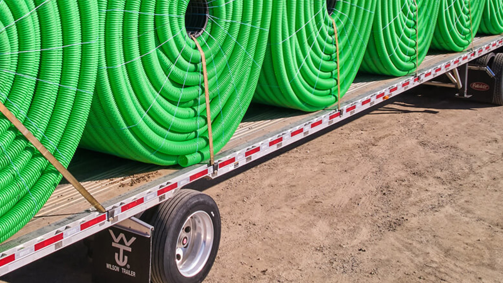 Coils of green tubing secured on a flatbed trailer.